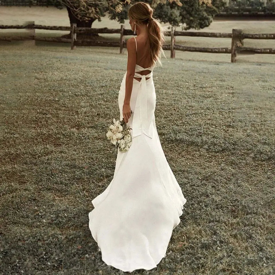 Custom Bohemian Wedding Dress showcased on a bride holding a bouquet in a serene outdoor setting.Custom Bohemian wedding dress with straps and open back
